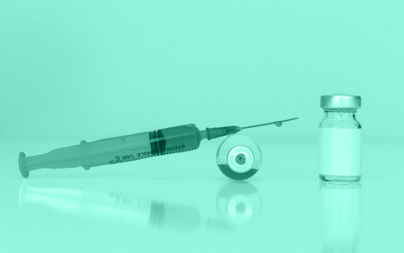 ein pharmazeutisches Vial liegt seitlich auf dem Boden und eine rote gefüllte Glasspritze liegt darauf