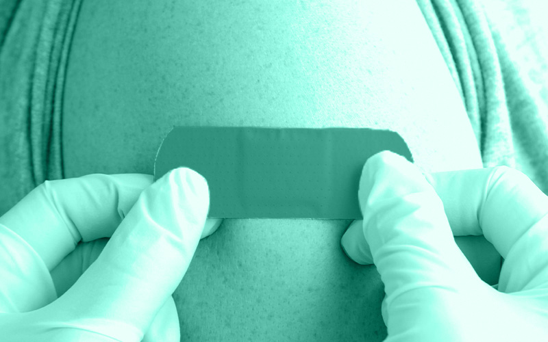 Ein Pflaster wird mit zwei Händen auf den Oberarm eines Mannes geklebt 