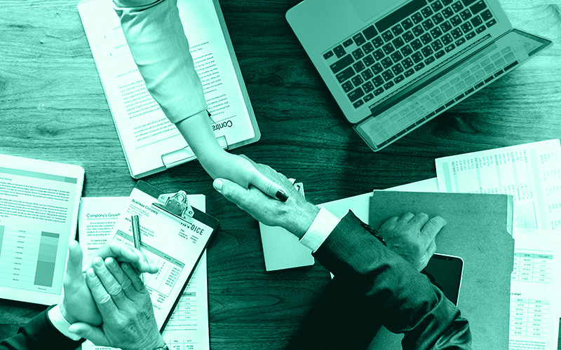 Zwei die sich am Tisch gegenübersitzen besiegeln per Handschlag einen Vertrag